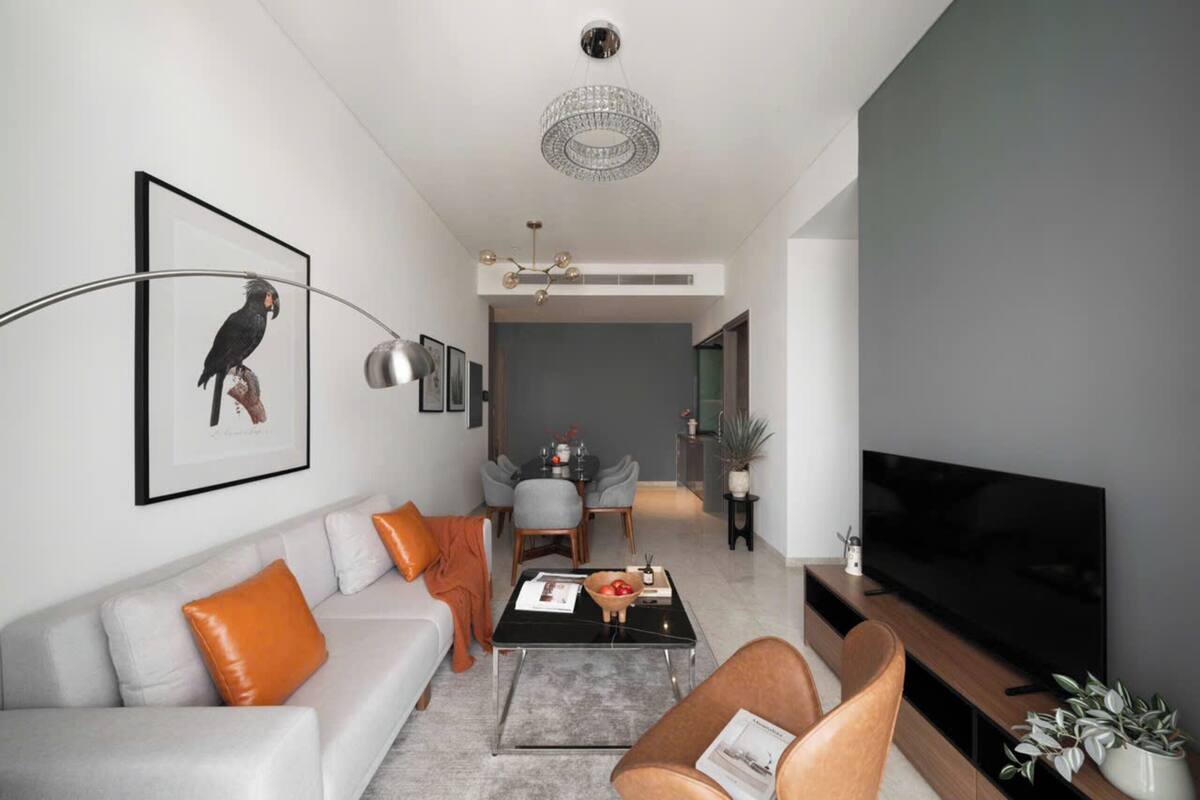 A modern living room with a sofa, coffee table, and television. There is a dining area with chairs and a table in the background.