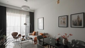 Ένα μοντέρνο σαλόνι με έναν καναπέ, πολυθρόνες, ένα τραπεζάκι σαλονιού και ένα τραπέζι τραπεζαρίας διαμορφωμένο για δύο άτομα.