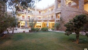 A multi-story hotel with a courtyard featuring a swimming pool, outdoor seating, and lush greenery. - Deoki Niwas Palace (Jaisalmer)