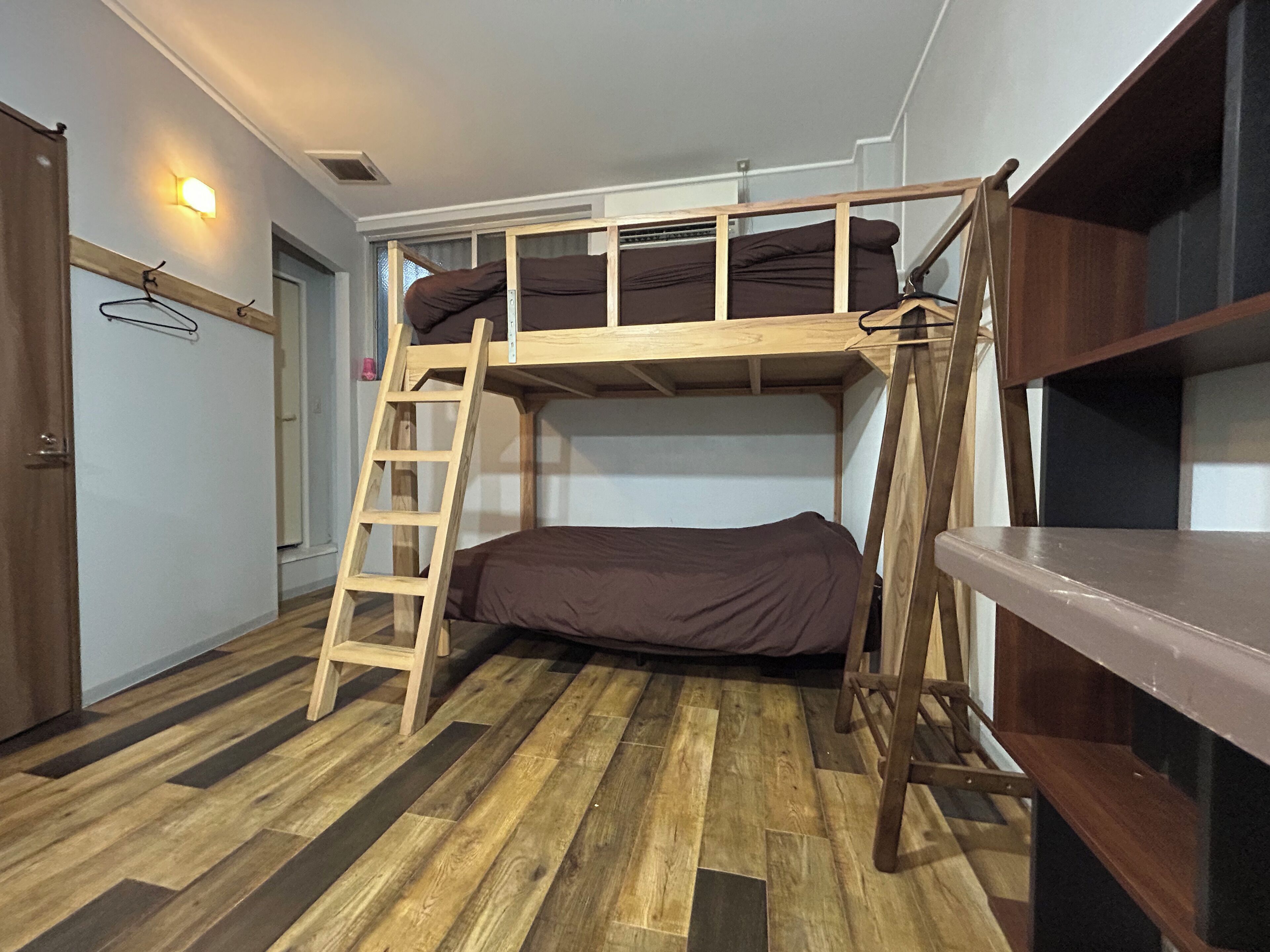 Una cama litera con escalera de madera, un escritorio de madera y un armario en una habitación con piso de madera.