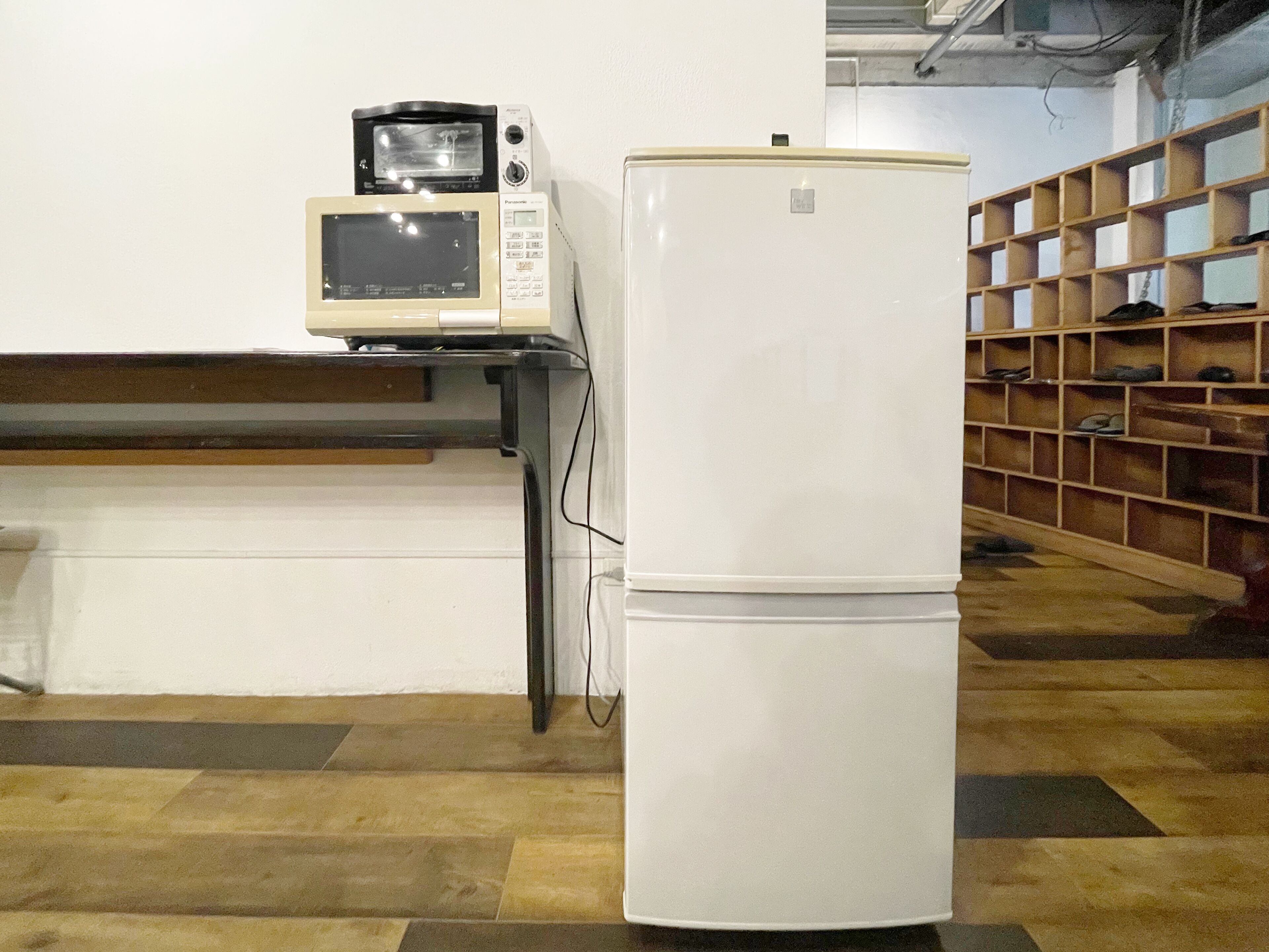 A kitchen with a microwave, a refrigerator, and a wooden shoe rack.
