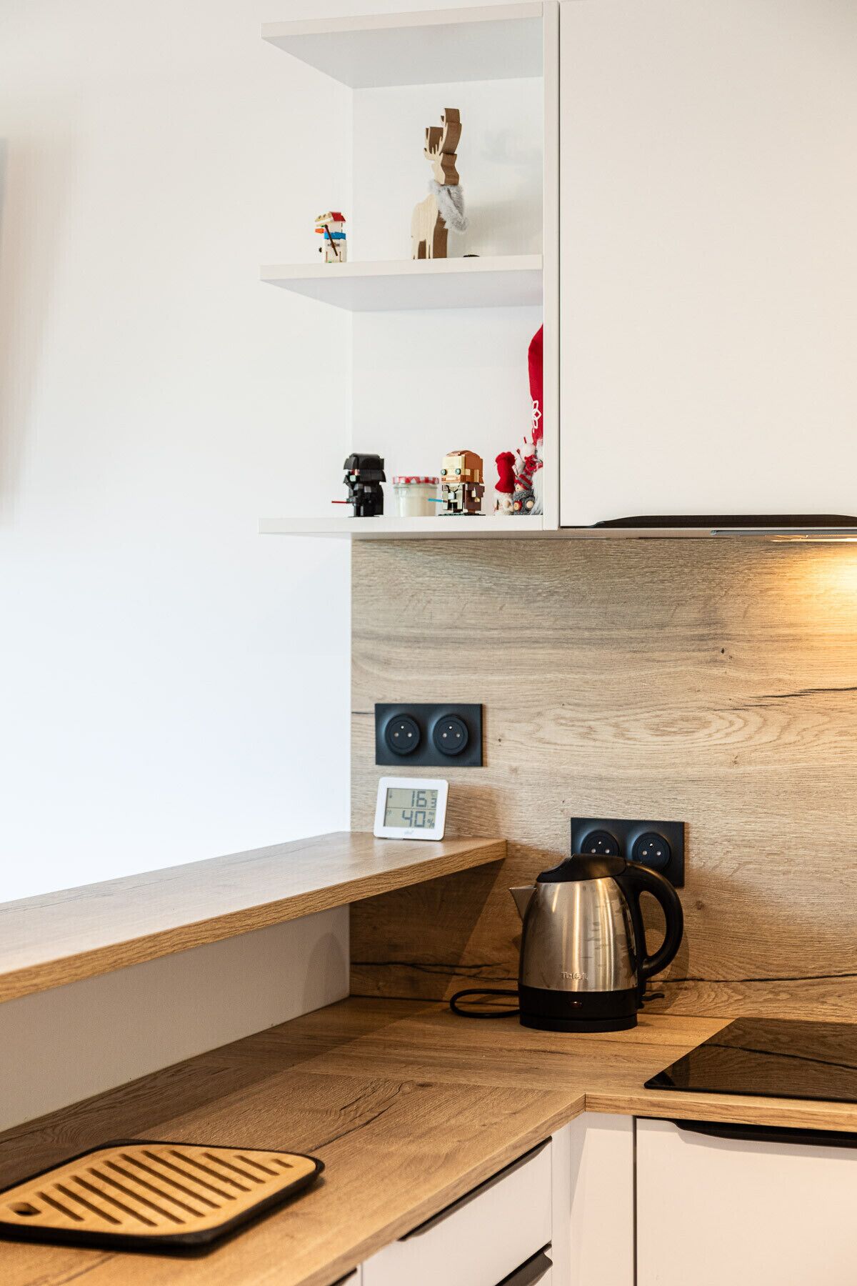 Une cuisine avec un plan de travail en bois, une bouilloire, une horloge numérique et un haut-parleur fixé au mur.