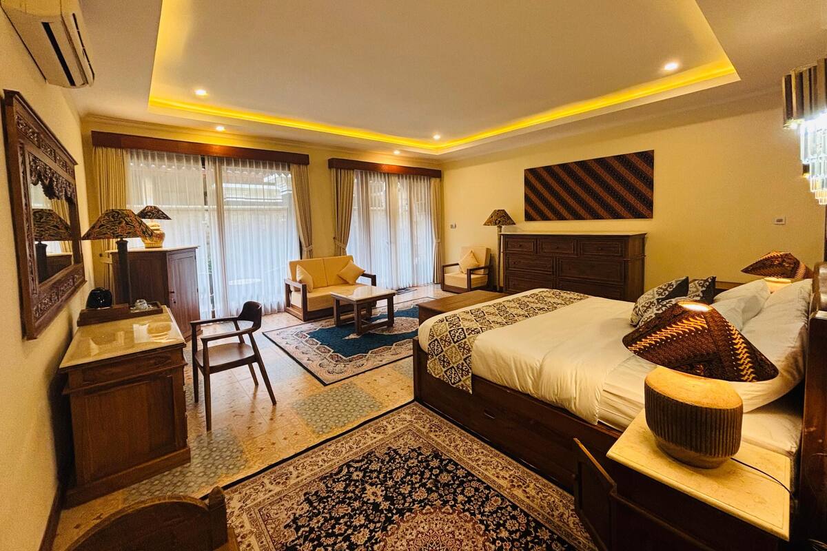A hotel room with a bed, a sofa, a chair, a desk, and a large window with curtains.