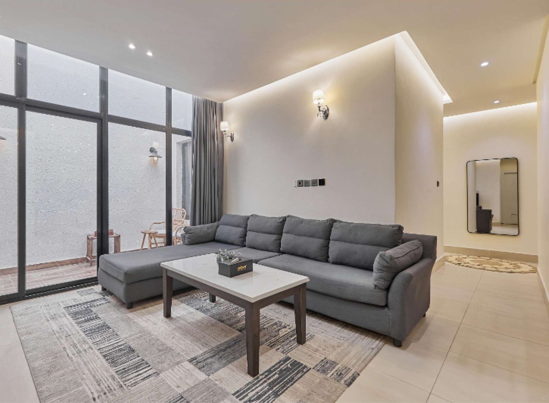 A modern living room with a grey sectional sofa, a coffee table, and a large window with curtains.