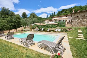 A pool with lounge chairs, a stone building, and a garden with trees and shrubs.