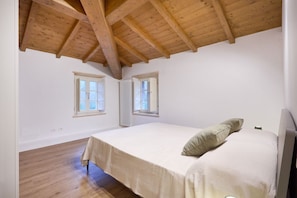 Un dormitorio con techo de madera, dos ventanas, un radiador y una cama con almohada.