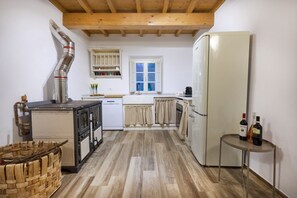 Una cocina compacta con estufa, horno y refrigerador, vigas de madera en el techo y un ventanal con cortinas.
