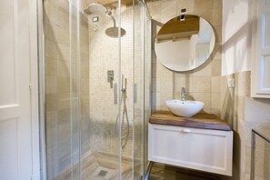 A modern bathroom with a glass-enclosed shower, a wooden vanity with a white sink, and a round mirror on the wall.