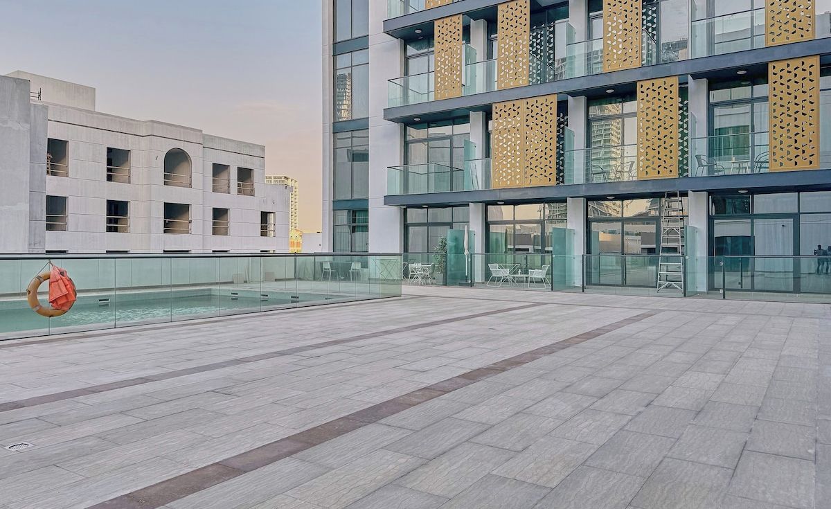 A modern hotel exterior with a spacious outdoor area, a pool, and a glass facade.