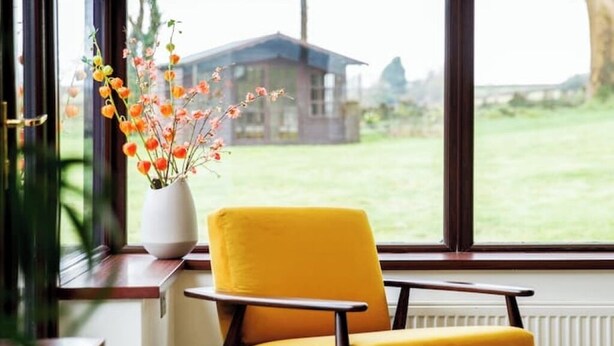 A yellow chair by a window with a view of a house and a lawn. - The Granary - Rustic Retreats (Reynoldston)