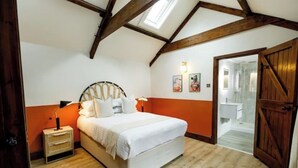 A bedroom with a bed, a nightstand, a wooden ceiling, and a door leading to another room. - The Granary - Rustic Retreats (Reynoldston)
