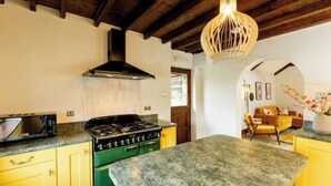 A kitchen with a stove, microwave, and wooden ceiling beams. - The Granary - Rustic Retreats (Reynoldston)
