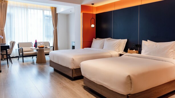 A hotel room with two beds, a desk, a chair, and a small table with a fruit bowl and wine glasses. - Jiuding Joy Hotel (Kathmandu)