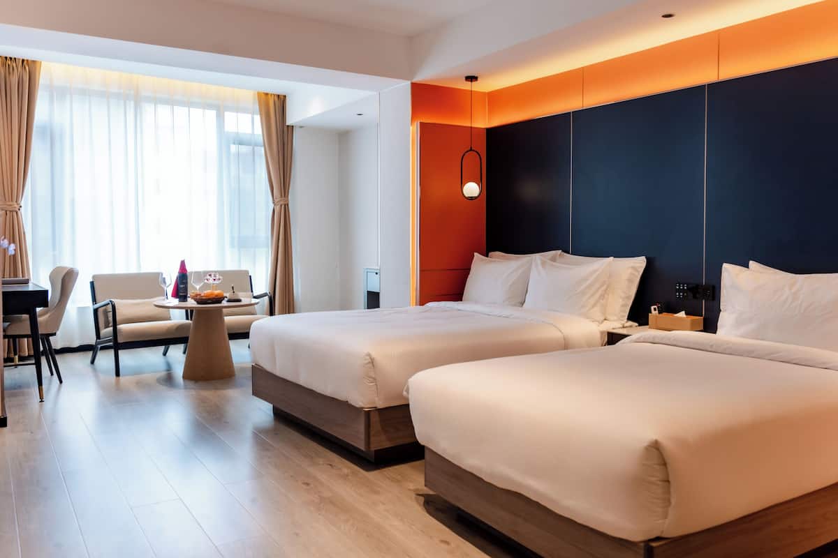Hotelkamer met twee bedden, een bureau, een stoel en een tafeltje met een schaal fruit en wijnglazen.