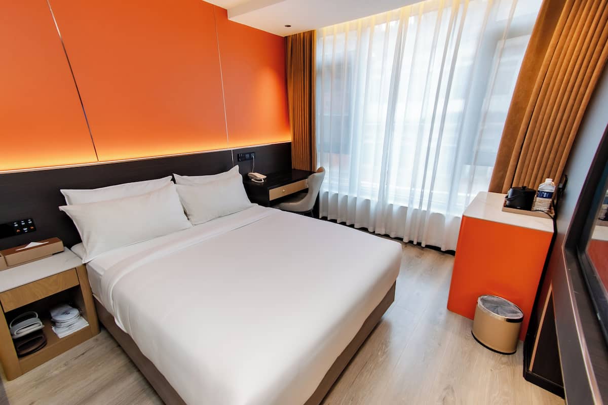Een hotelkamer met een groot bed, een nachtkastje met telefoon, een klein bureau en een prullenbak.