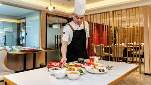 A chef preparing food in a modern restaurant with a clean, minimalist interior and a dining area visible in the background. - Jiuding Joy Hotel (Kathmandu)