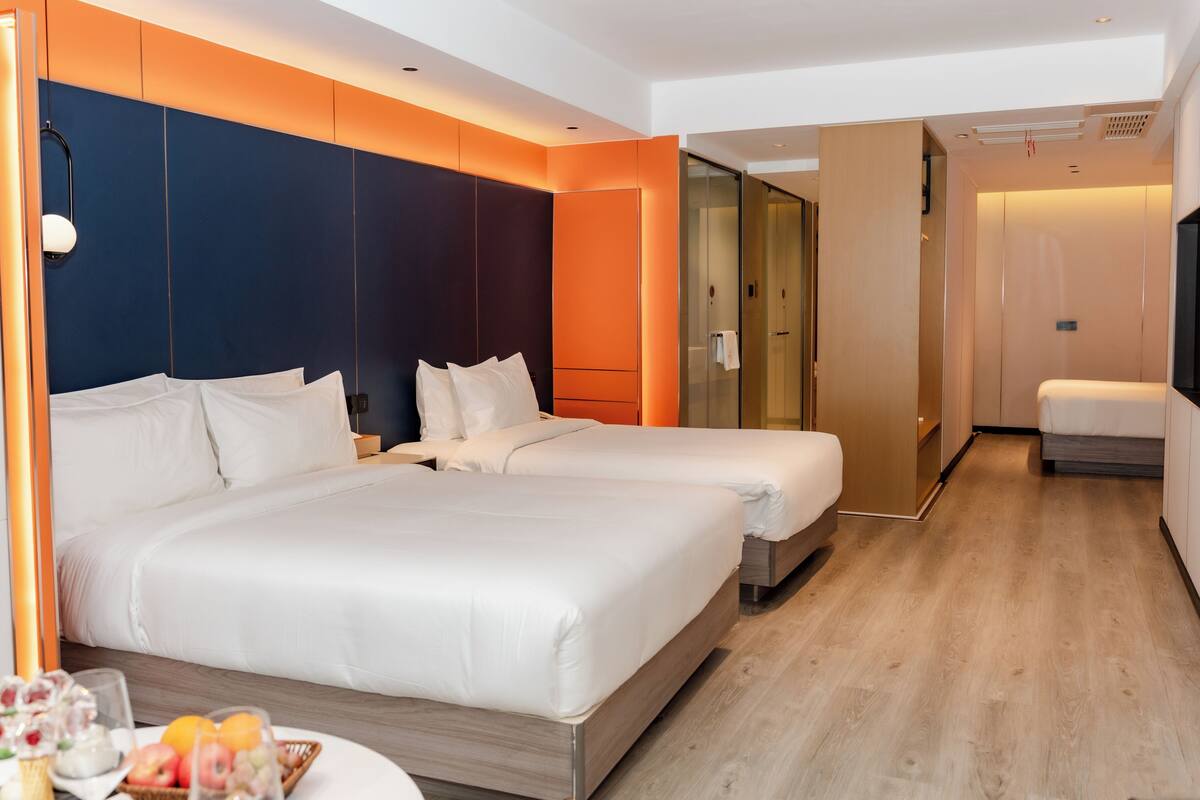 Een hotelkamer met twee bedden, een tafeltje met fruit, een spiegel en een inloopkast.