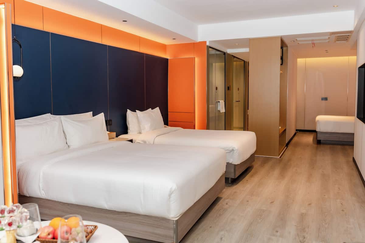 Habitación de hotel con dos camas, una mesita con fruta, un espejo y un vestidor.
