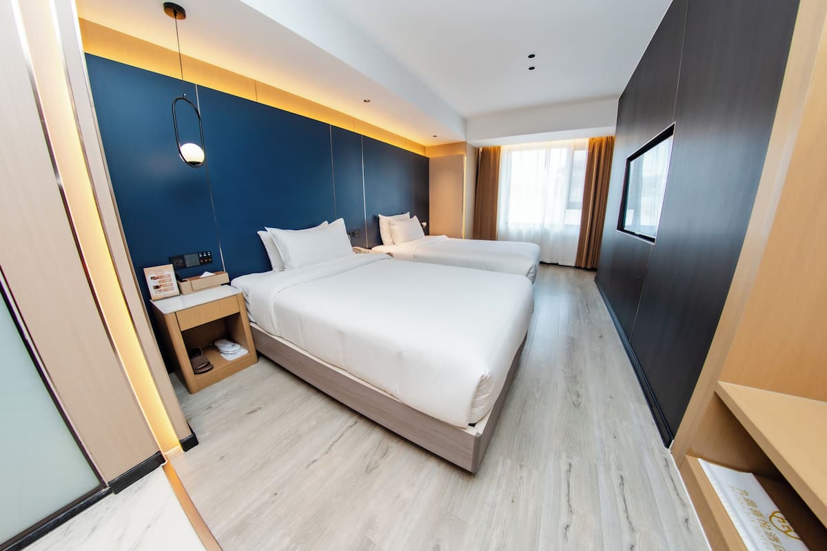 Una habitación de hotel moderna con una cama grande, mesitas de noche, un armario y un ventanal con cortinas.