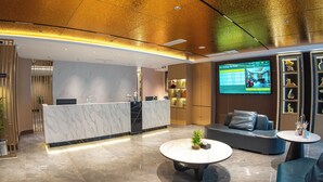 A hotel lobby with a reception desk, seating area, and a TV screen displaying hotel information. - Jiuding Joy Hotel (Kathmandu)