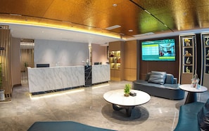 A hotel lobby with a reception desk, seating area, and a TV screen displaying hotel information. - Jiuding Joy Hotel (Kathmandu)