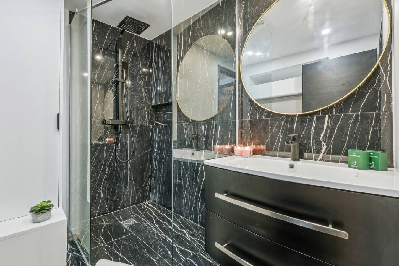 A modern bathroom with a glass shower enclosure, a large mirror, and a vanity with a marble countertop.