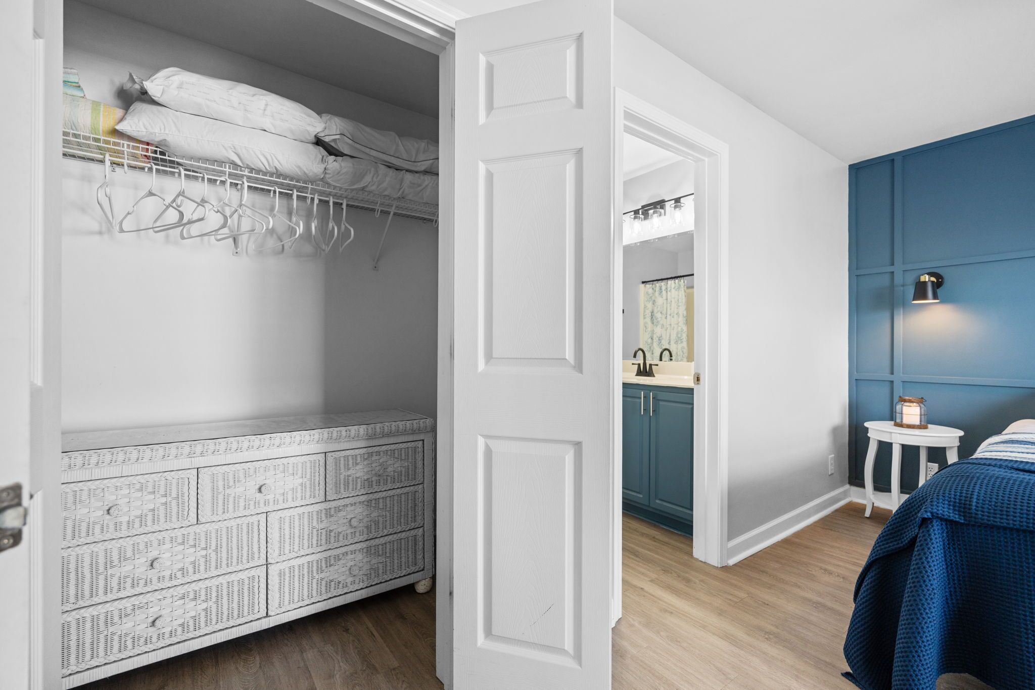 Une chambre avec un lit superposé, une commode, une petite table avec une lampe, et une salle de bain avec un lavabo et un miroir.