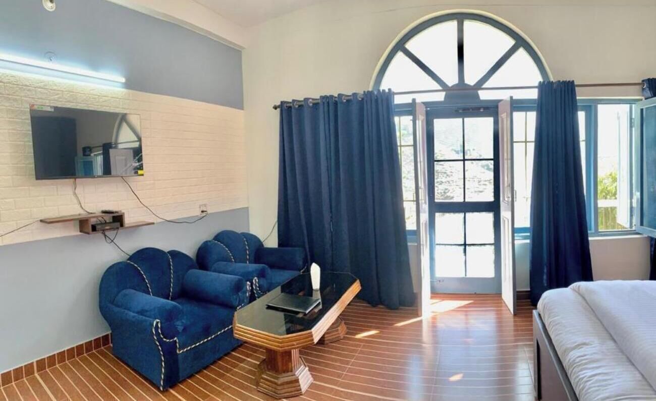 A room with a sofa, a bed, a TV mounted on the wall, and a large window with curtains.