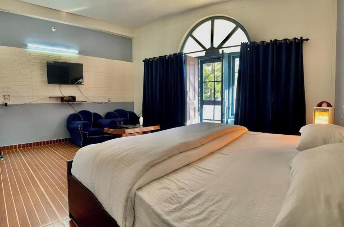 A hotel room with a large bed, a TV mounted on the wall, a desk with a chair, and a window with curtains.