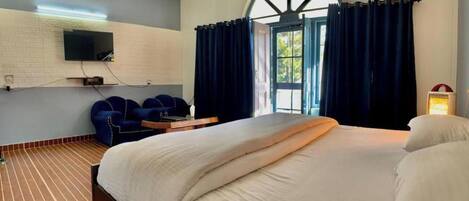 A hotel room with a large bed, a TV mounted on the wall, a desk with a chair, and a window with curtains.