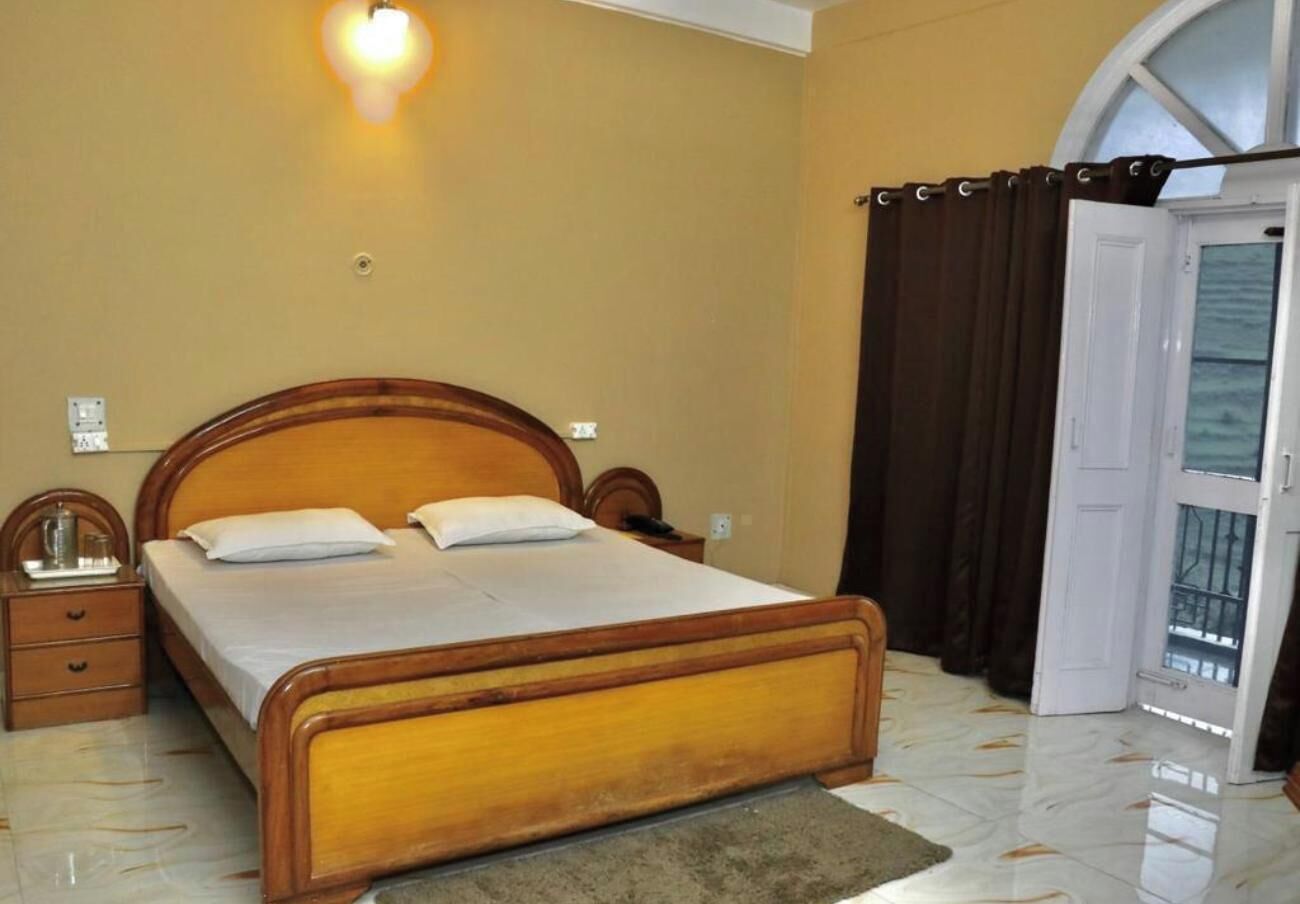 A bedroom with a wooden bed, a nightstand, a lamp, and a window with curtains.