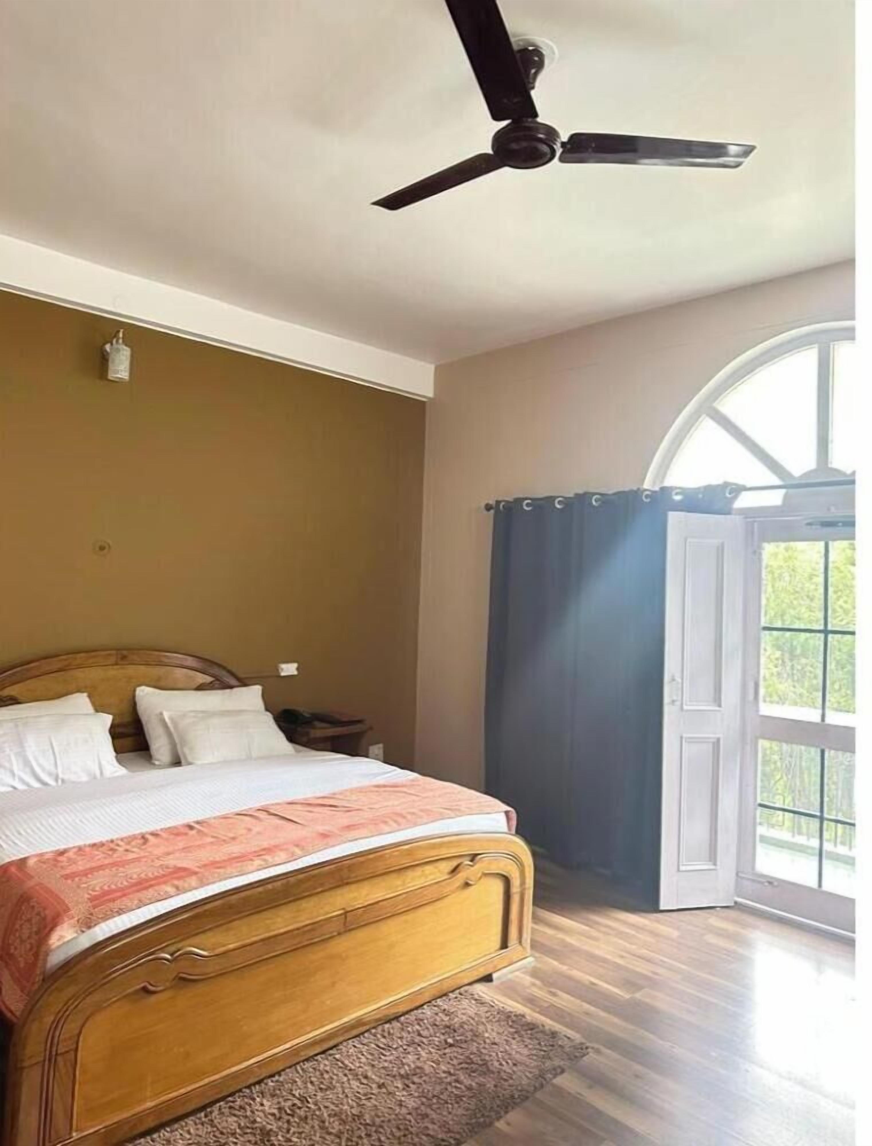 A bedroom with a wooden bed, a ceiling fan, a nightstand, and a large window with curtains.
