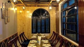 A long dining table set for a meal in a room with wooden walls and ceiling, large windows, and a chandelier.
