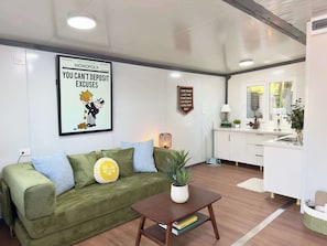 A living room with a green sofa, a coffee table, a framed poster, a cabinet, and a window.