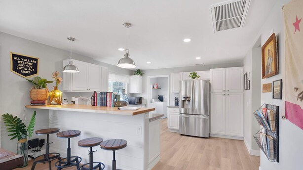 Una cocina moderna con armarios blancos, una isla central con taburetes, electrodomésticos de acero inoxidable e iluminación colgante.