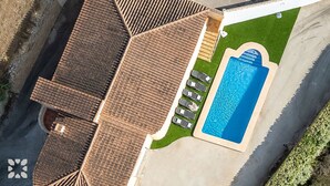 Vista aérea de una propiedad residencial con piscina, terraza cubierta y césped cuidado.