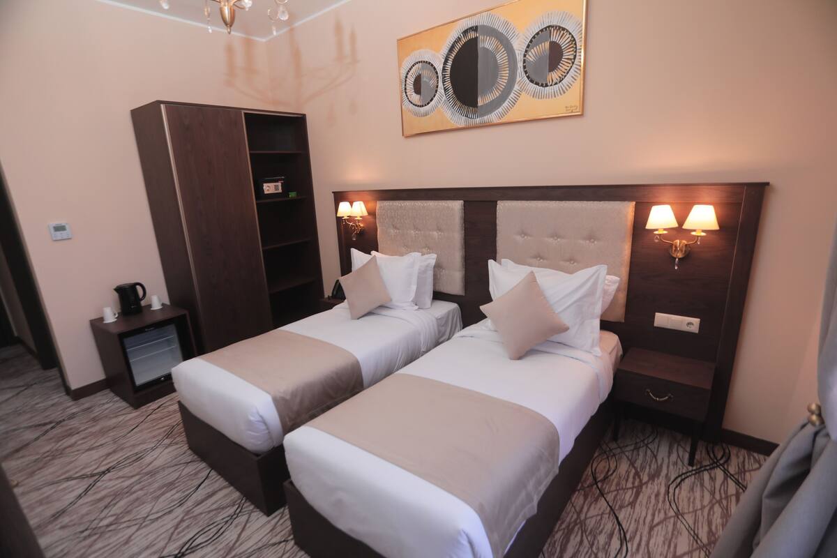 Une chambre d’hôtel avec deux lits, une armoire, une table de chevet et une œuvre d’art accrochée au mur.