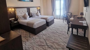 Une chambre d’hôtel avec deux lits, un bureau, une chaise, une télévision et un tableau au mur.