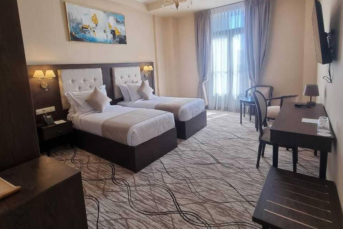 Une chambre d’hôtel avec deux lits, un bureau, une chaise, une télévision et un tableau au mur.