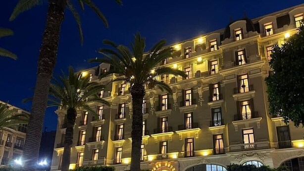 Un hôtel à plusieurs étages doté de balcons, de palmiers et d’un éclairage chaleureux.