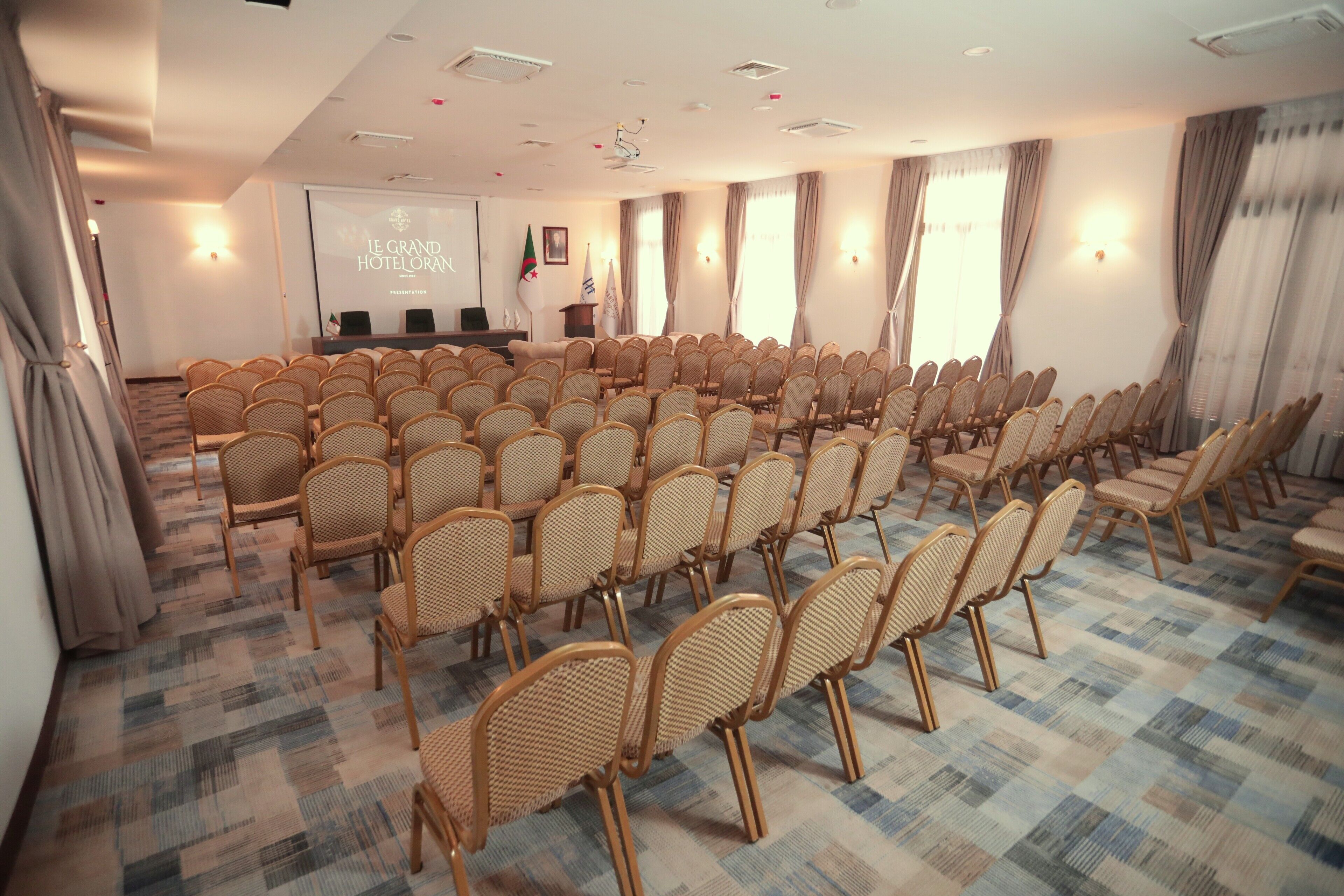 A conference room with rows of wicker chairs, a projection screen, and a podium.