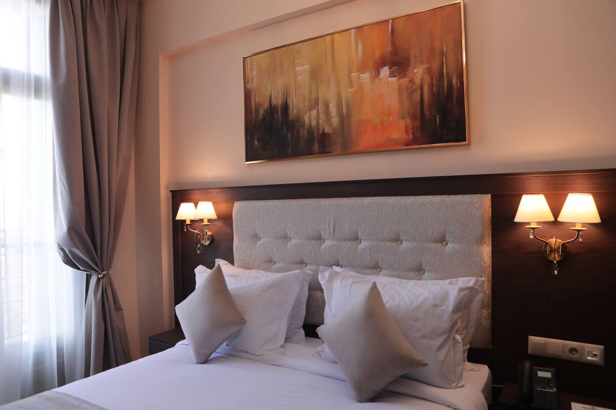 Une chambre d’hôtel avec un grand lit, deux lampes de chevet, une tête de lit et un tableau au mur.