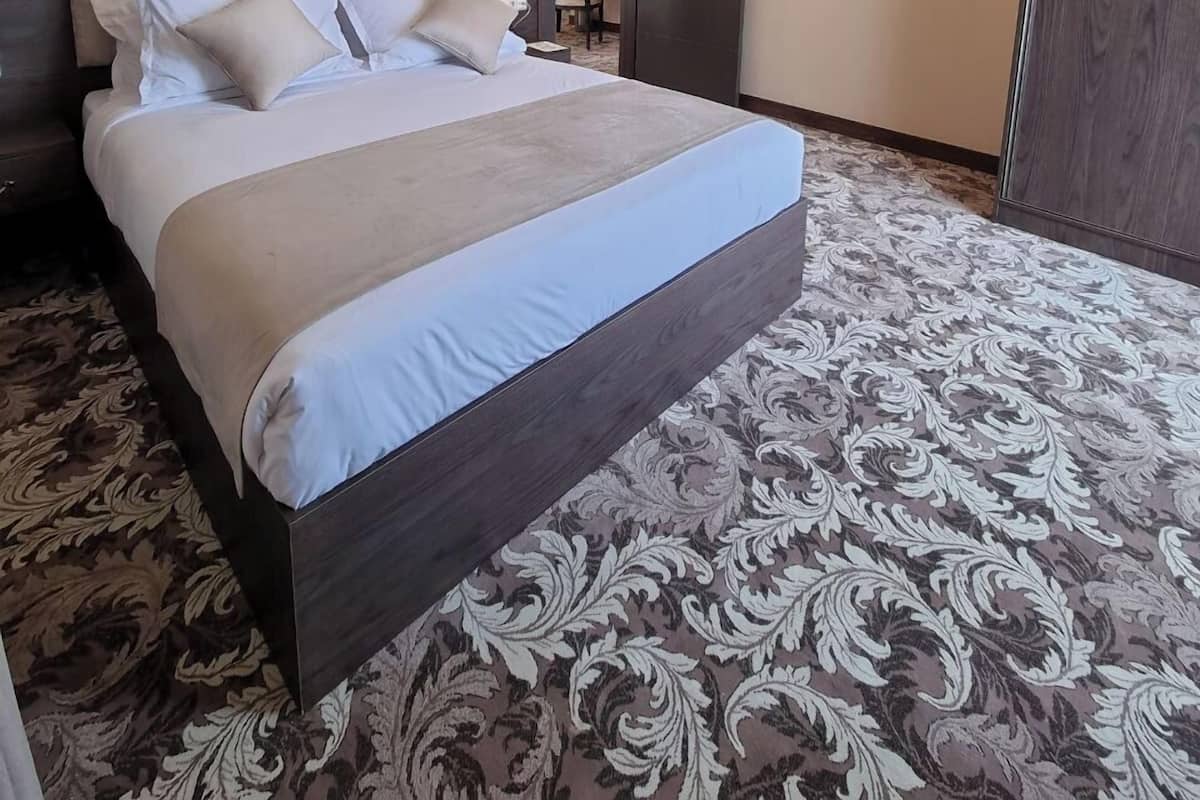 Un grand lit avec une tête de lit sombre, un lustre, un tableau au mur et une moquette à motifs.