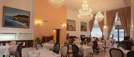 Un comedor con mesas dispuestas para el servicio, candelabros y obras de arte en las paredes.
