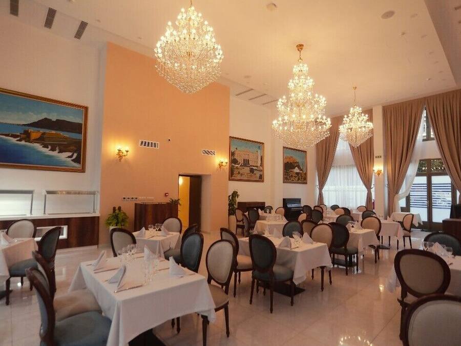 A dining area with tables set for service, chandeliers, and artwork on the walls.