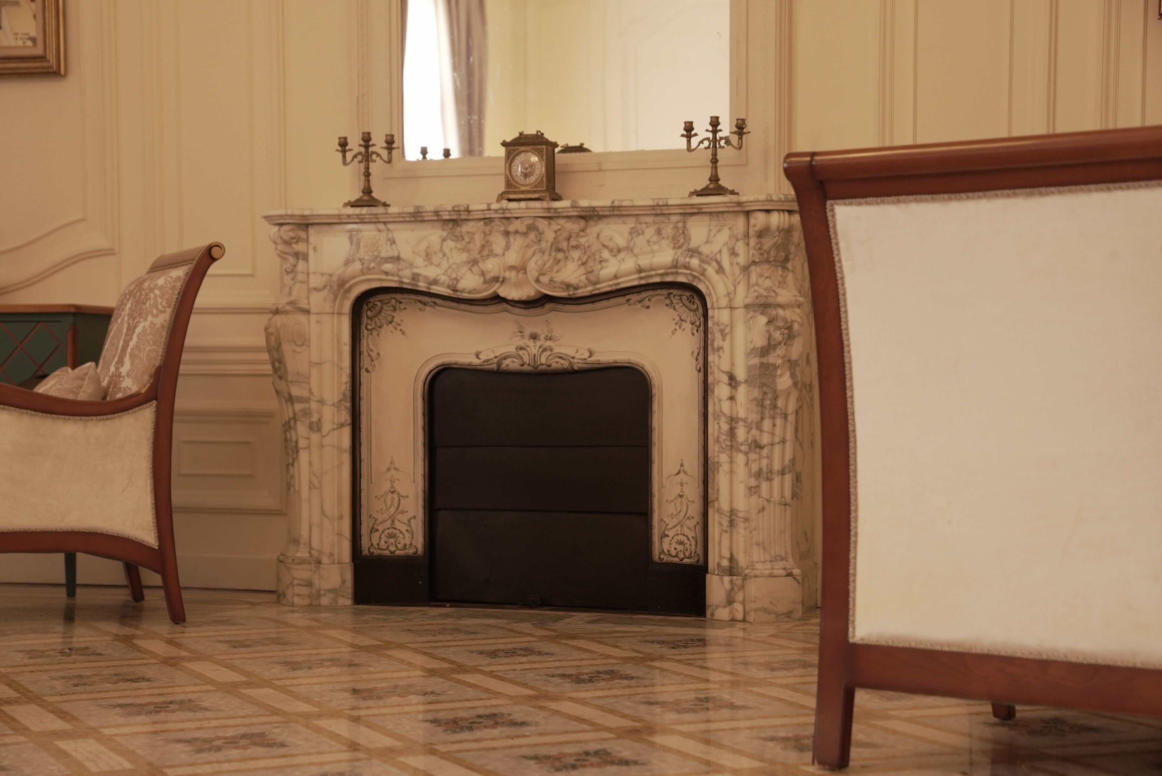 Una habitación con chimenea de mármol, una silla de madera y una cama con estructura de madera.