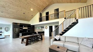 A spacious living area with a high ceiling, a staircase, a dining area, and a kitchen. - Spa, River, Pool Table | Chalet Ombre & Lumière (Entrelacs)
