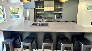 A modern kitchen with a central island, bar stools, and pendant lighting. - Spa, River, Pool Table | Chalet Ombre & Lumière (Entrelacs)