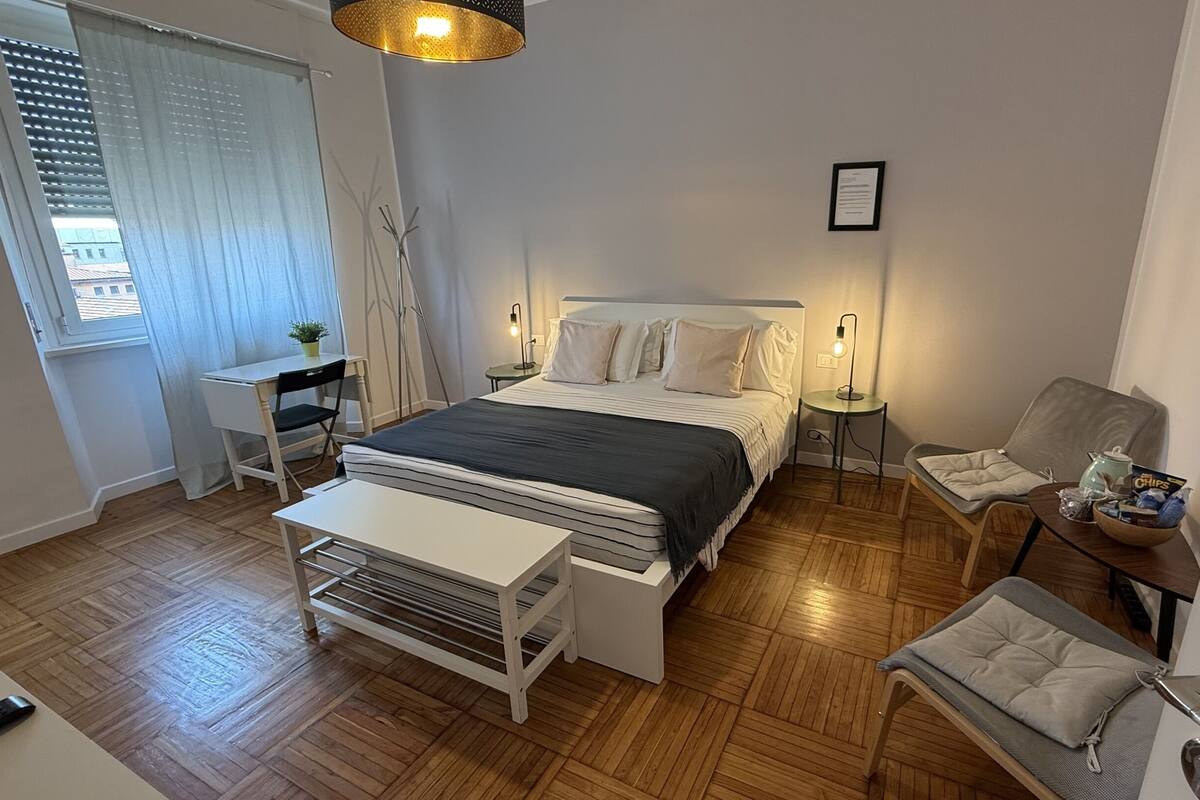 A bedroom with a bed, bedside tables, a desk, a chair, and a small table with snacks.
