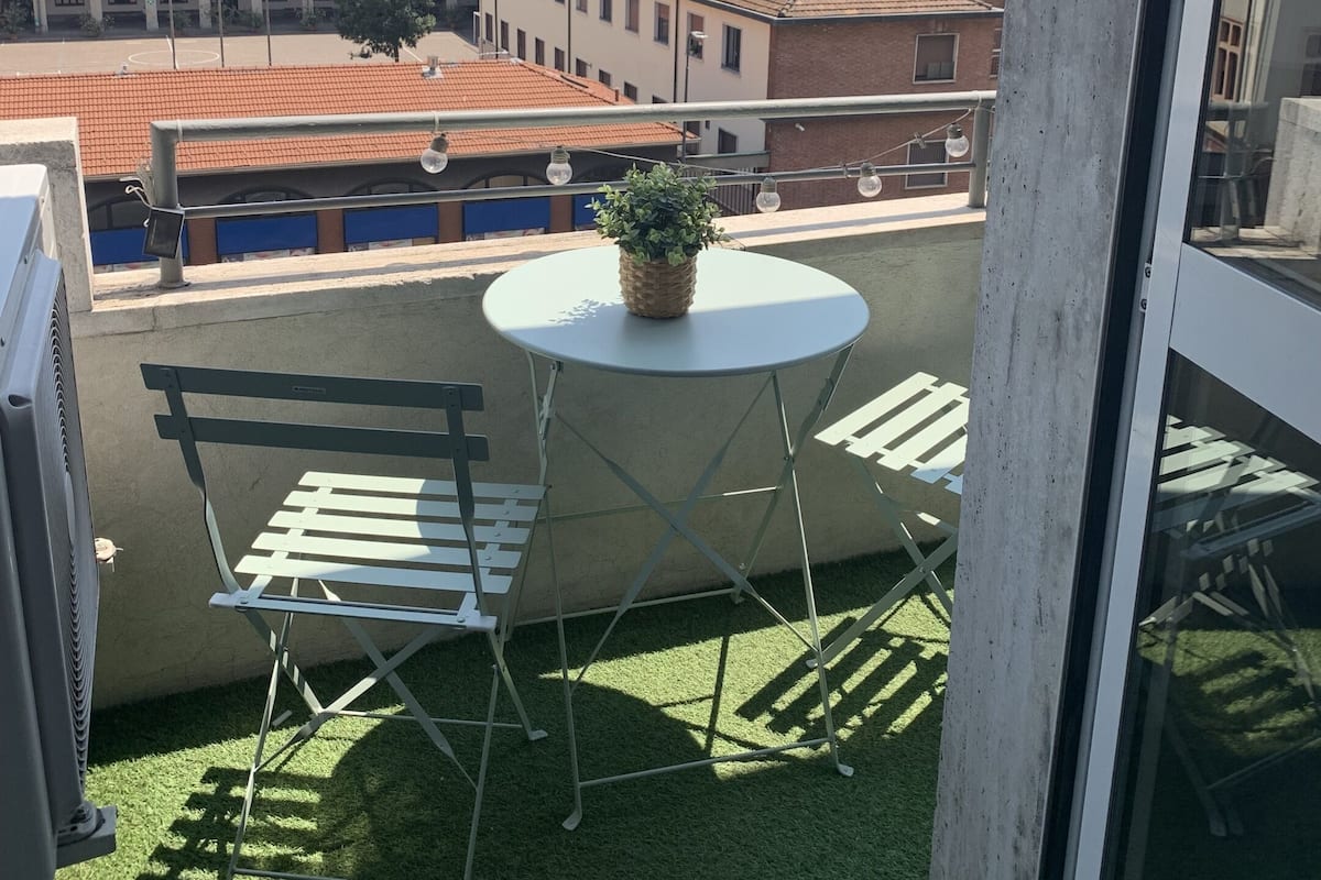 A balcony with a table and two chairs, a potted plant, and a view of city buildings.